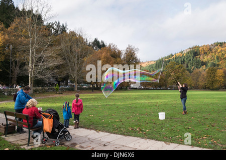 Eine Frau macht eine große bunte Blase, während Kinder am Dorfanger in Betws-y-Coed Conwy North Wales UK Großbritannien beobachten Stockfoto