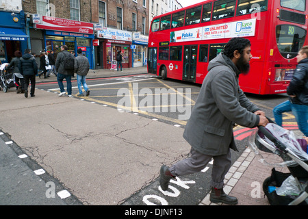 Fußgänger Mann Kinderwagen überquert befahrene Straße Grays Inn Road mit roten Doppeldecker Bus Busse Autos Verkehr in King's Cross Bereich von London UK KATHY DEWITT Stockfoto