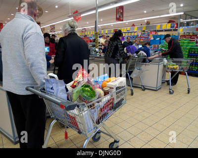 Kunden mit einem voll beladenen Einkaufswagen in der Warteschlange, um an der Kasse in Aldi Store in Wales, Großbritannien, zu bezahlen, KATHY DEWITT Stockfoto