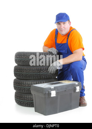 Mechaniker blauen Overalls und orange T-shirt erschossen von Haufen von vier neue Autoreifen und Toolbox posiert auf weiß Stockfoto