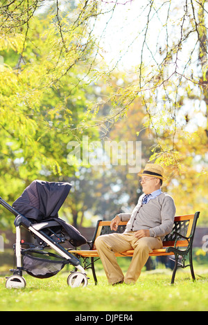 Ältere Mann auf einer Bank sitzend und mit Blick auf seinen Neffen Baby im Kinderwagen Stockfoto