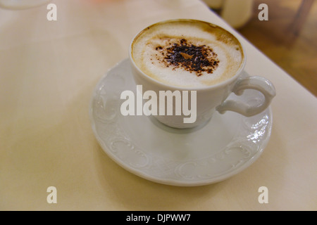 Tasse Cappuccino mit aufgeschäumter Milchschaum, garniert mit Schokopulver.  Einfache Tan Tabelle. Stockfoto