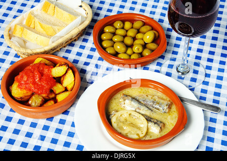 Spanische Tapas-Auswahl von Sardinen in Zitronensauce, Patatas Bravas, grünen Oliven und ein Glas Rotwein. Stockfoto