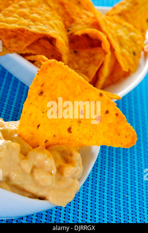Nahaufnahme einer Schüssel mit Tortilla-Chips, eingetaucht in Nacho Käse auf blauem Hintergrund Stockfoto