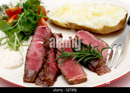 Closeup auf Scheiben von gegrillten Gourmet-Wagyu Rib-Eye-Steak mit Meerrettichsauce, gebackene Kartoffeln und einen frischen grünen Salat serviert Stockfoto