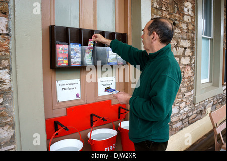 Mann unter Zug Fahrplan & Flugblätter im Churston Bahnhof, Devon, England. Stockfoto