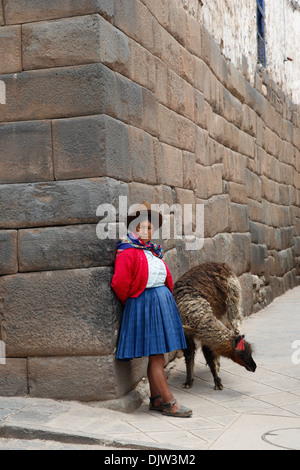 Quechua-Frau mit Lama entlang einer Inka-Wand in San Blas Nachbarschaft, Cuzco, Peru. Stockfoto