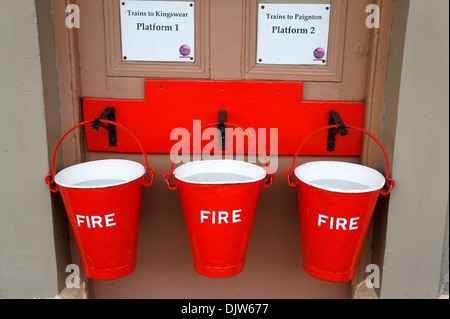 Nahaufnahme von roten Feuer Eimer voller Wasser auf Gleis 1 am Bahnhof Churston, Devon, England. Stockfoto