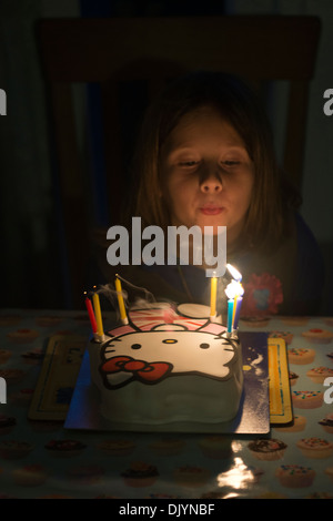 Ein junges Mädchen feiert ihren Geburtstag durch Ausblasen der Kerzen auf ihrem Geburtstagskuchen. Stockfoto