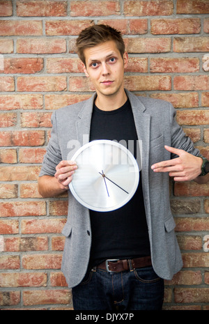 Junger Geschäftsmann hält eine Uhr auf Ziegel Wand Hintergrund. Zeit in Business-Konzept Stockfoto