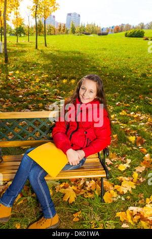 Herbst Porträt ein 11 Jahre altes Mädchen sitzen auf der Bank im Park nach der Schule mit Papierordner Stockfoto
