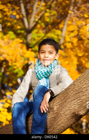 Schwarz 10 Jahre alten schwarzen Jungen sitzen auf dem Baum im Herbst park Stockfoto