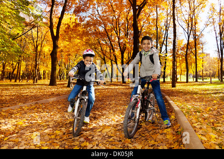 Zwei schwarze 8 und 10 Jahre alten Jungen fahren Fahrrad, Helm im Herbst Ahorn und Eiche Baum-park Stockfoto