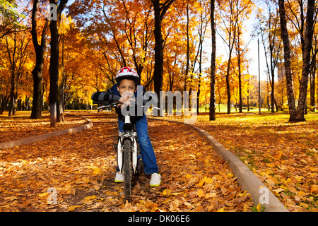 Glücklich lächelnd 8 Jahre schwarzer Junge mit dem Fahrrad in den Herbst Park gelehnt auf dem Fahrrad Heck Stockfoto