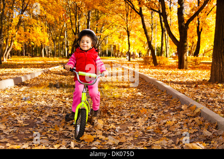 Kleine schwarze Mädchen mit dem Fahrrad im Park auf der Straße bedeckt mit Herbst Eiche und Ahorn Bäumen Stockfoto