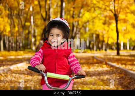 Enge Porträt von kleinen schwarzen Mädchen mit dem Fahrrad im Park auf der Straße mit Herbst Eiche und Ahorn Bäumen bedeckt Stockfoto