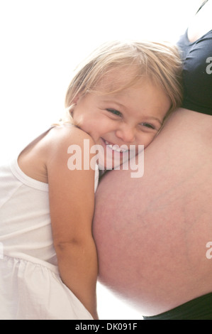 Eine Herr kaukasischen Mutter lässt ihre zwei-jährige kaukasische Herr Tochter "hören" ihre Baby-Schwester während einer Porträt-Sitzung in ihrer Stockfoto