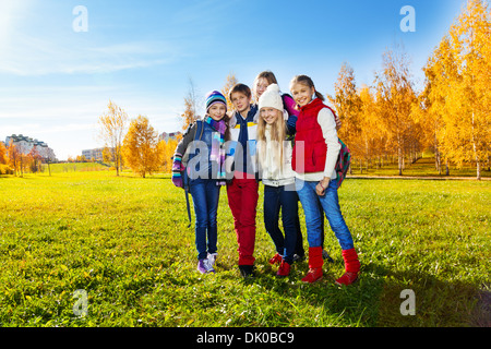 Gruppe von fünf glückliche Kinder, Jungen und Mädchen im Park stehen nach der Schule tragen warme Kleidung mit Rucksäcken an sonnigen Herbsttag Stockfoto