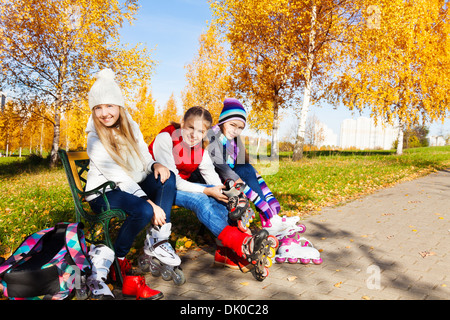 Drei glückliche Mädchen setzen auf Rollerblades sitzen im park Stockfoto