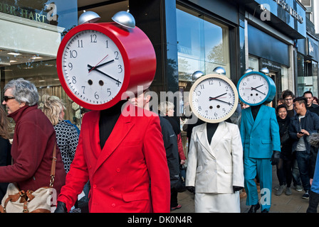 Drei Personen gekleidet in roten, weißen und blauen Anzügen mit Uhren für Köpfe zu Fuß entlang der Princes Street in Edinburgh. Stockfoto
