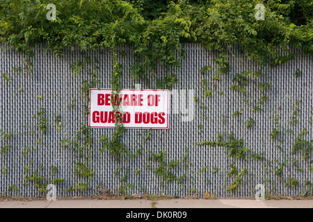 Schild mit der Aufschrift "Vorsicht vor der Wachhunde" Warnung montiert auf einem überwucherten Zaun. Stockfoto