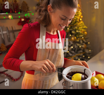 Glückliche junge Hausfrau macht Apple in Schokoladenglasur in Weihnachten eingerichtet Küche Stockfoto