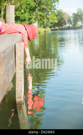 Kleines Mädchen am Steg liegen, den Blick auf das Wasser und Griff nach ihrem eigenen Spiegelbild, Schweden Stockfoto
