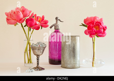 Stillleben mit rosa Pfingstrosen in Vasen neben Selters Flasche und Silber-Container Stockfoto