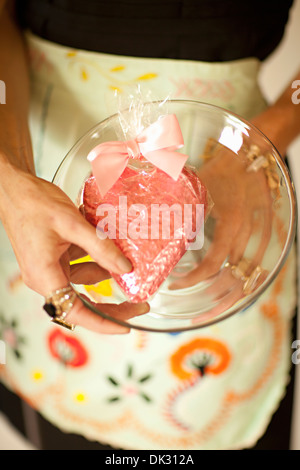 Erhöhte Ansicht schließen eingewickelt Mittelteil Frau in Schürze Holding Herzform Valentinstag Cookie auf klare Kuchenplatte Stockfoto