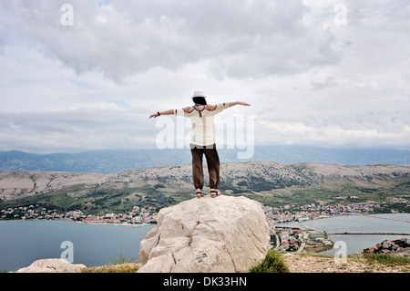 Mitte Erwachsene Frau mit ausgestreckten Armen auf Felsen mit Blick auf die Stadt Pag, Insel Pag, Kroatien, Europa Stockfoto