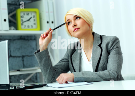 Junge schöne nachdenkliche Geschäftsfrau am Tisch sitzen und das Nachschlagen im Büro Stockfoto