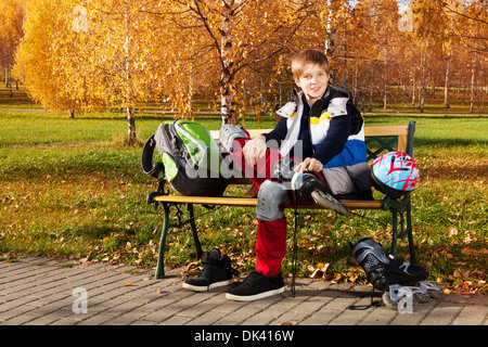 10 Jahre alten Schuljunge sitzt auf der Bank im Herbst Park mit Rollerblades