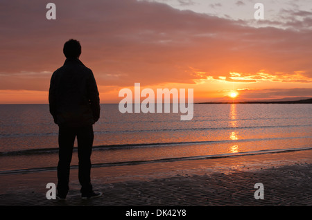 Mann, Blick auf das Meer bei einem wunderschönen Sonnenuntergang in Troon Stockfoto