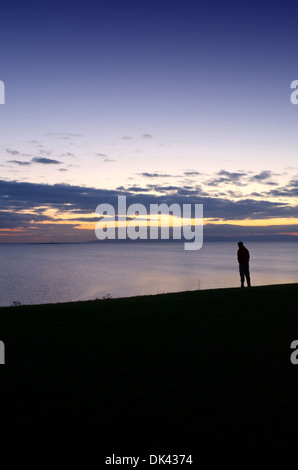 Ein einsamer Mann steht am Rand einer Klippe dramatischen Sonnenuntergang in Troon an der Westküste von Schottland Stockfoto