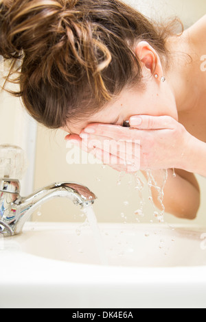 Junge Frau im Nachthemd waschen Gesicht im Waschbecken im Bad Stockfoto