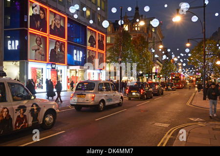 Oxford Street West End of London Taxis stehen in der Shopping Street Szene vor Gap Bekleidungsgeschäft Nacht beleuchtete Weihnachtsdekoration England Großbritannien Stockfoto