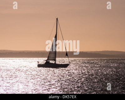 Silhouette einer Yacht auf dem Solent am Abend mit der Isle Of Wight im Hintergrund Stockfoto