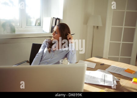 Junge Geschäftsfrau in Gedanken beim Sitzen an ihrem Schreibtisch mit Laptop wegsehen. Schöne junge Frau, die von zu Hause aus arbeiten Stockfoto