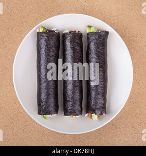 Drei Sushi-Rollen in Nori Algen gewickelt auf Platte, über hölzerne Hintergrund. Stockfoto