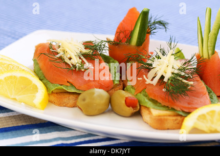 Sandwiches mit Lachs, Käse, Salat, Kräuter auf Teller, Oliven und Zitronen. Stockfoto