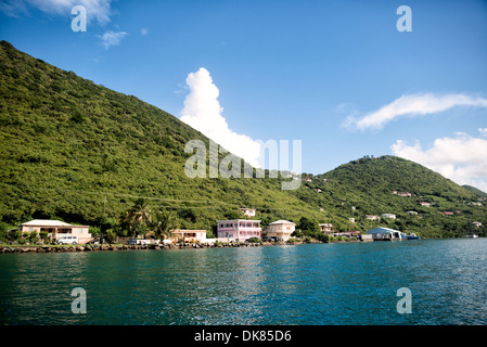 West End Waterfront Tortola BVI / WEST END, British Virgin Islands — pastellfarbene Häuser säumen die felsengepanzerte Küste von West End, Tortolas westlichste Siedlung, die vom Wasser aus vor dicht bewaldeten Vulkanhügeln blickt. West End dient als Hauptfährhafen, der Tortola mit St. John und St. Thomas auf den benachbarten U.S. Virgin Islands verbindet, was es zum primären Tor für Reisen zwischen den Inseln in diesem Teil der Karibik macht. Stockfoto