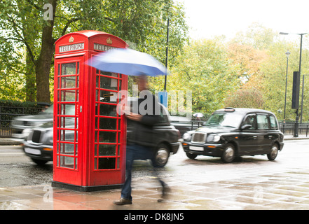 Rote Telefon Kabine in London. Mann mit Regenschirm Stockfoto