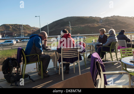 Kunden, die bei einer Tasse Kaffee in der Sonne im Freien auf der Terrasse in einem Café am Meer in Saltburn am Meer im Herbst Stockfoto