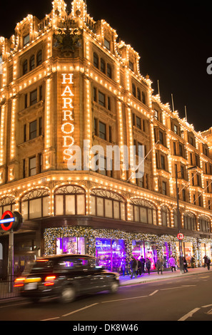 Das Kaufhaus Harrods. Fassade in der Nacht beleuchtet. Taxi-Pässe vor dem Gebäude Stockfoto