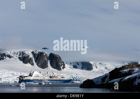 Antarktis, Petermann Island Cruise Schiff verankert in der Nähe vergletscherte Berge in der Nähe von Lemaire-Kanal am sonnigen Abend Stockfoto