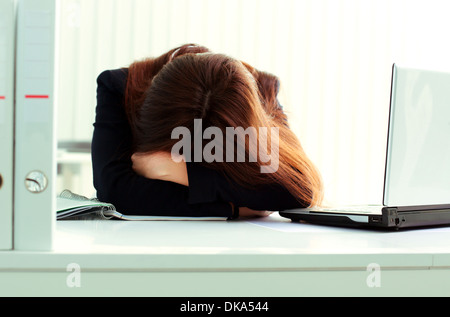 Junge müde Geschäftsfrau, die an ihrem Arbeitsplatz im Büro schlafen Stockfoto