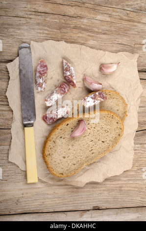 Salami, Knoblauch und Brot auf einem alten Küchentisch Stockfoto