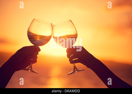 Mann und Frau klingende Weingläser mit Champagner bei Sonnenuntergang dramatischer Himmelshintergrund Stockfoto