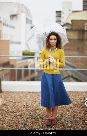 Weibliche Büroangestellte auf Dach hält Regenschirm Stockfoto