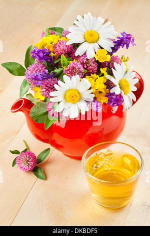 rote Teekanne mit Bouquet von heilenden Kräutern und Blumen, gesunde Tee auf Tisch, Kräutermedizin Stockfoto